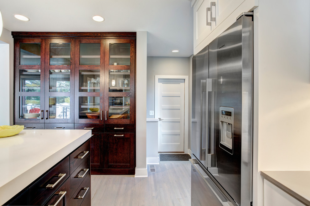 Photo of a medium sized contemporary l-shaped kitchen/diner in Minneapolis with a submerged sink, white cabinets, quartz worktops, white splashback, glass tiled splashback, stainless steel appliances, medium hardwood flooring and an island.