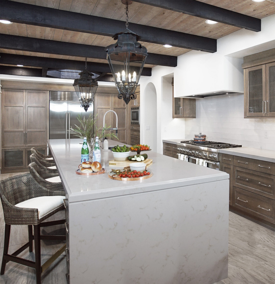 Inspiration for a medium sized traditional enclosed kitchen with a submerged sink, recessed-panel cabinets, brown cabinets, engineered stone countertops, white splashback, ceramic splashback, stainless steel appliances, travertine flooring, an island, grey floors, grey worktops and a wood ceiling.