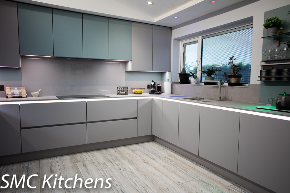 Medium sized modern u-shaped kitchen/diner in Other with a built-in sink, flat-panel cabinets, grey cabinets, laminate countertops, grey splashback, stone slab splashback, integrated appliances, porcelain flooring, a breakfast bar, grey floors, grey worktops and a vaulted ceiling.
