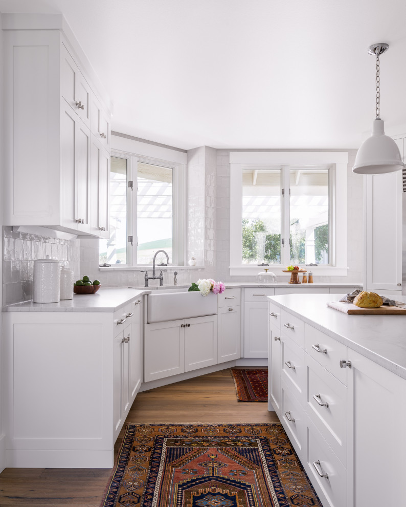 Inredning av ett klassiskt avskilt, stort grå grått u-kök, med en rustik diskho, skåp i shakerstil, vita skåp, bänkskiva i kvartsit, grått stänkskydd, stänkskydd i keramik, rostfria vitvaror, mellanmörkt trägolv, en köksö och brunt golv