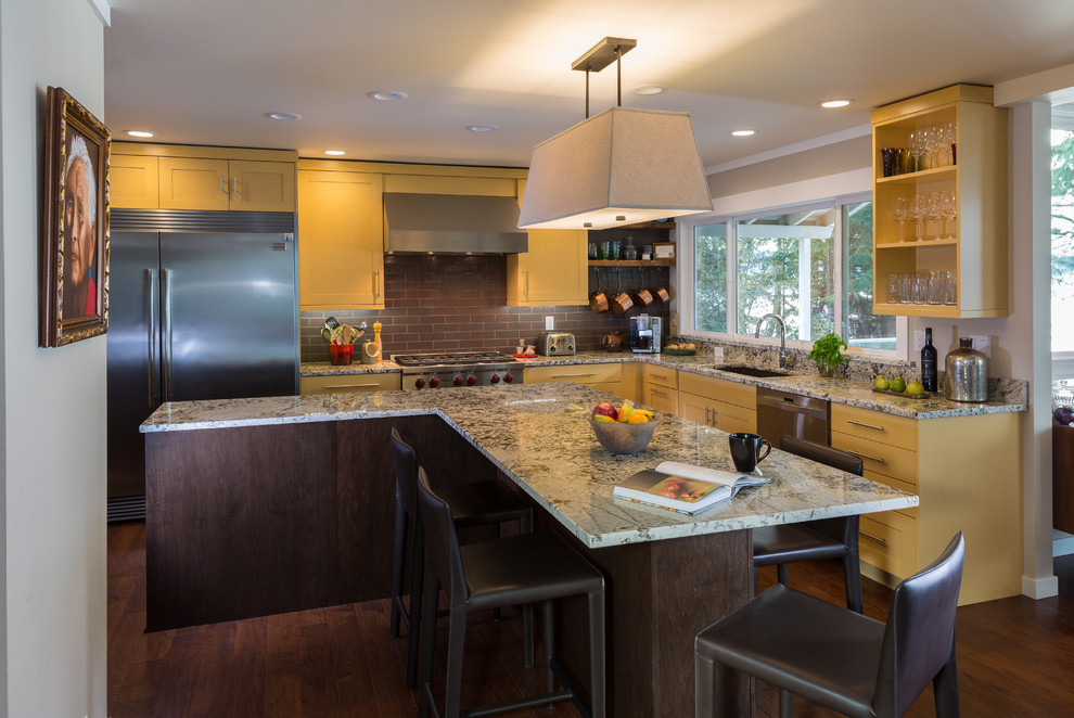 Photo of a medium sized retro l-shaped open plan kitchen in Seattle with a submerged sink, shaker cabinets, yellow cabinets, engineered stone countertops, red splashback, stainless steel appliances, dark hardwood flooring, an island, brick splashback and brown floors.