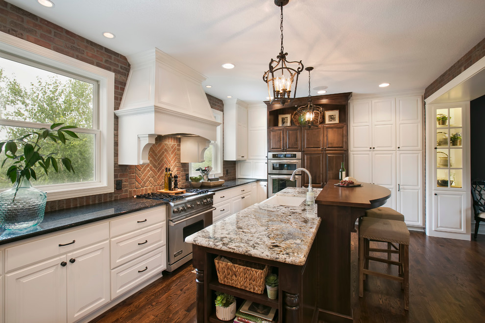 Inspiration for a mid-sized timeless u-shaped dark wood floor and brown floor eat-in kitchen remodel in Minneapolis with a farmhouse sink, raised-panel cabinets, white cabinets, granite countertops, red backsplash, brick backsplash, stainless steel appliances, an island and multicolored countertops