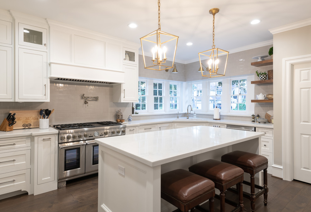 Photo of a classic l-shaped kitchen in Houston with a submerged sink, shaker cabinets, white cabinets, grey splashback, metro tiled splashback, stainless steel appliances, medium hardwood flooring, an island, brown floors and white worktops.