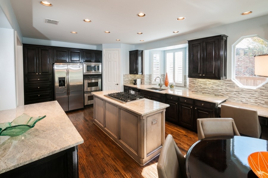 Inspiration for a transitional medium tone wood floor eat-in kitchen remodel in Dallas with a drop-in sink, raised-panel cabinets, dark wood cabinets, granite countertops, gray backsplash and stainless steel appliances
