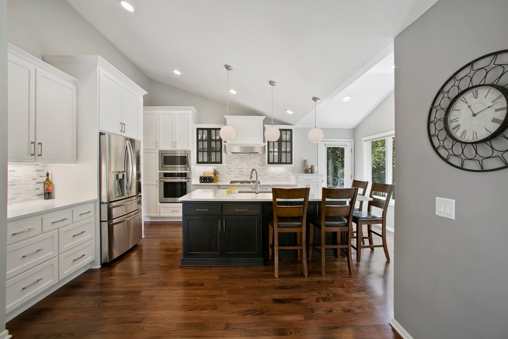 Example of a transitional medium tone wood floor kitchen design in Minneapolis with an undermount sink, flat-panel cabinets, white cabinets, quartz countertops, white backsplash, mosaic tile backsplash, stainless steel appliances and an island