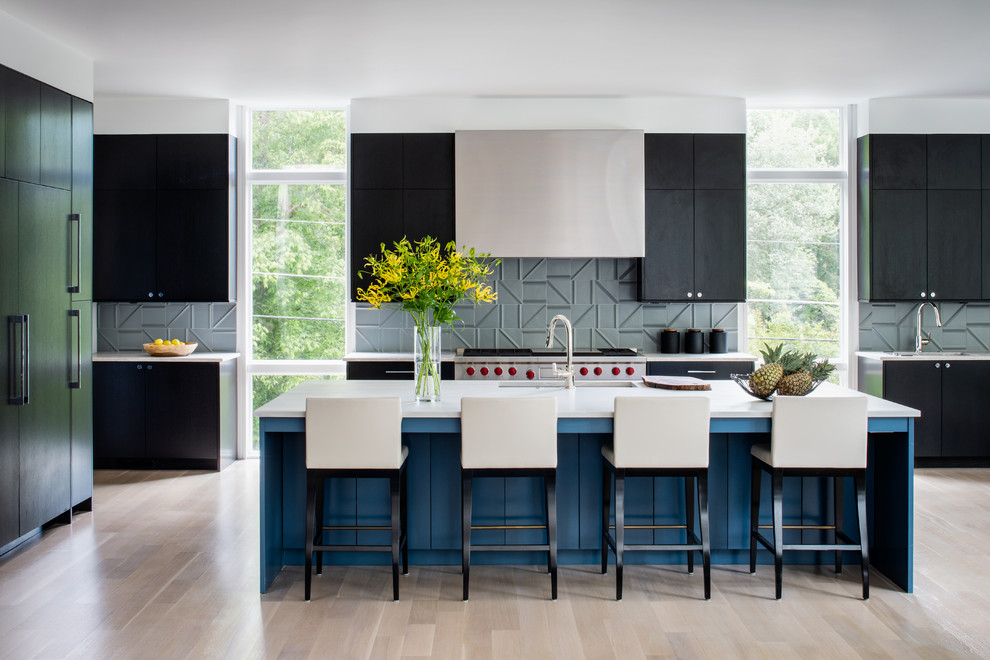 Foto di un cucina con isola centrale design con lavello sottopiano, ante lisce, ante nere, paraspruzzi grigio, elettrodomestici in acciaio inossidabile, parquet chiaro, pavimento beige e top bianco