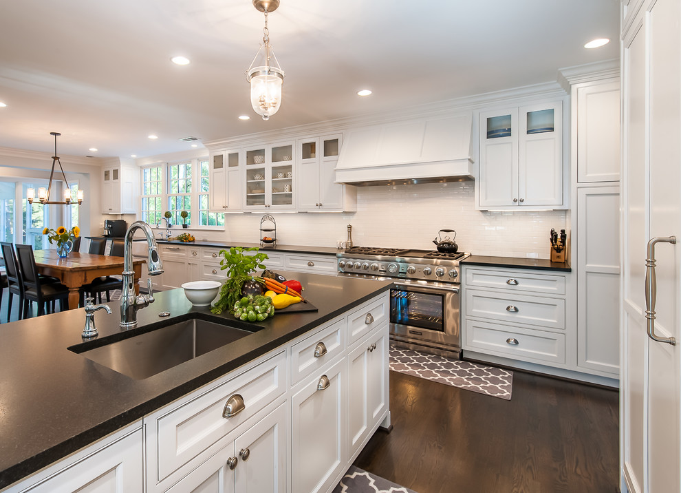 Open concept kitchen - large traditional l-shaped dark wood floor and brown floor open concept kitchen idea in DC Metro with a farmhouse sink, recessed-panel cabinets, white cabinets, quartz countertops, white backsplash, ceramic backsplash, stainless steel appliances and an island