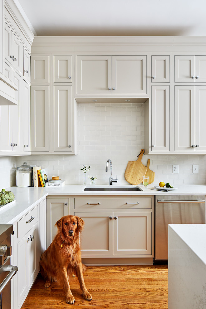 Eat-in kitchen - mid-sized traditional u-shaped medium tone wood floor eat-in kitchen idea in DC Metro with beige cabinets, white backsplash, subway tile backsplash, stainless steel appliances, an island and white countertops