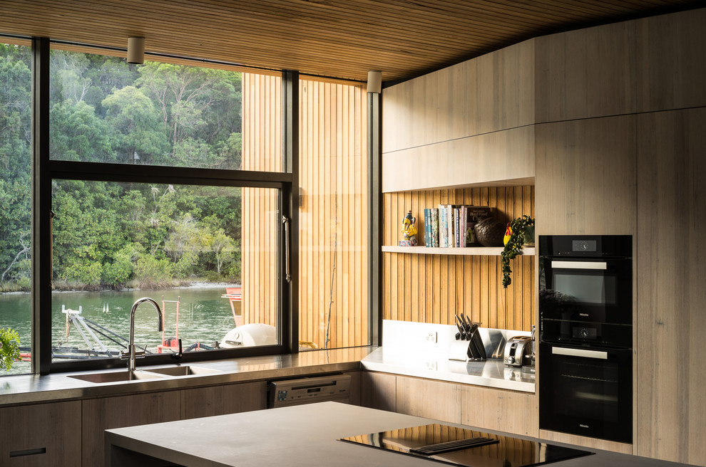 Design ideas for a contemporary l-shaped open plan kitchen in Sunshine Coast with black appliances, an island, a double-bowl sink, flat-panel cabinets, medium wood cabinets, window splashback and grey worktops.