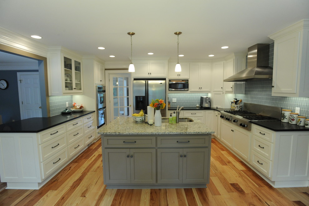 Foto på ett avskilt, stort vintage u-kök, med en undermonterad diskho, luckor med infälld panel, vita skåp, granitbänkskiva, brunt stänkskydd, stänkskydd i glaskakel, rostfria vitvaror, mellanmörkt trägolv och en köksö