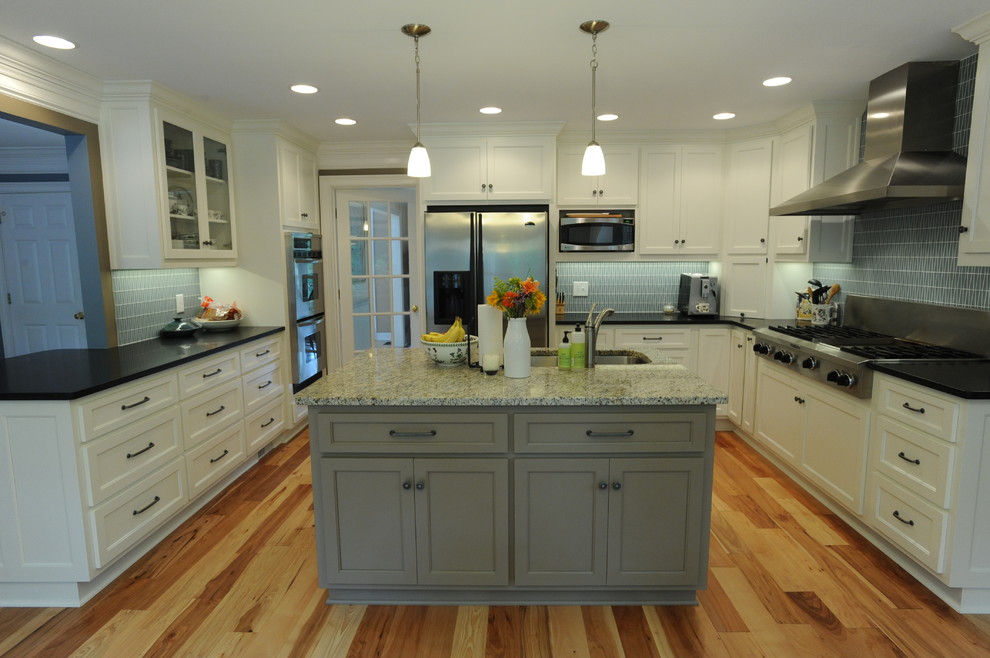 Inredning av ett klassiskt u-kök, med en undermonterad diskho, luckor med infälld panel, vita skåp, granitbänkskiva, brunt stänkskydd, stänkskydd i glaskakel, rostfria vitvaror, mellanmörkt trägolv och en köksö