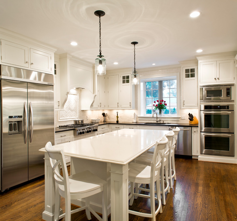 Bild på ett mellanstort lantligt kök, med en undermonterad diskho, luckor med infälld panel, vita skåp, granitbänkskiva, vitt stänkskydd, stänkskydd i porslinskakel, rostfria vitvaror, mörkt trägolv och en köksö