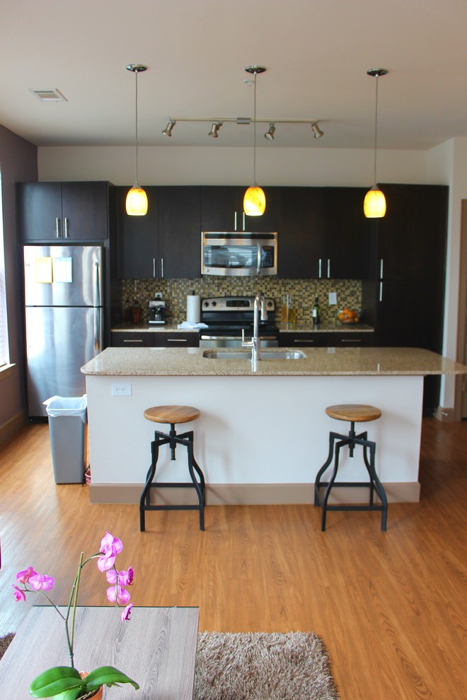 Example of a small urban single-wall medium tone wood floor open concept kitchen design in Dallas with a double-bowl sink, dark wood cabinets, granite countertops, green backsplash, stainless steel appliances, an island and flat-panel cabinets