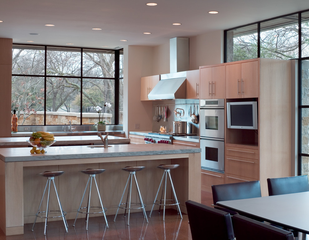Стильный дизайн: п-образная кухня в стиле модернизм с обеденным столом, монолитной мойкой, плоскими фасадами, светлыми деревянными фасадами и техникой из нержавеющей стали - последний тренд