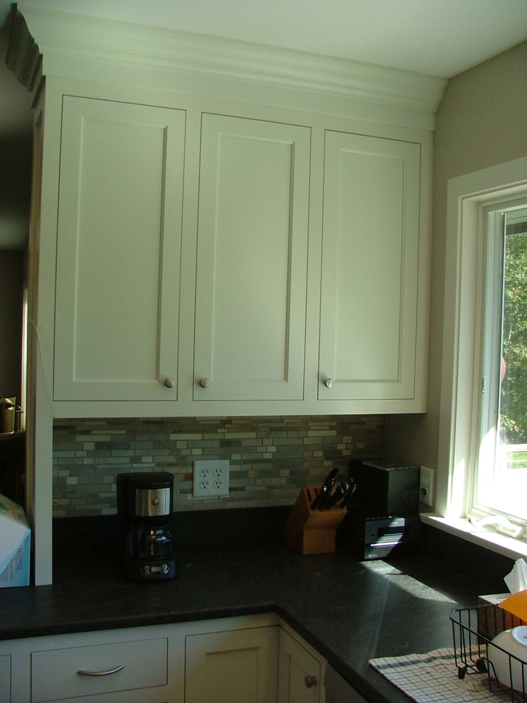 Klassisk inredning av ett kök, med en undermonterad diskho, luckor med infälld panel, vita skåp och granitbänkskiva