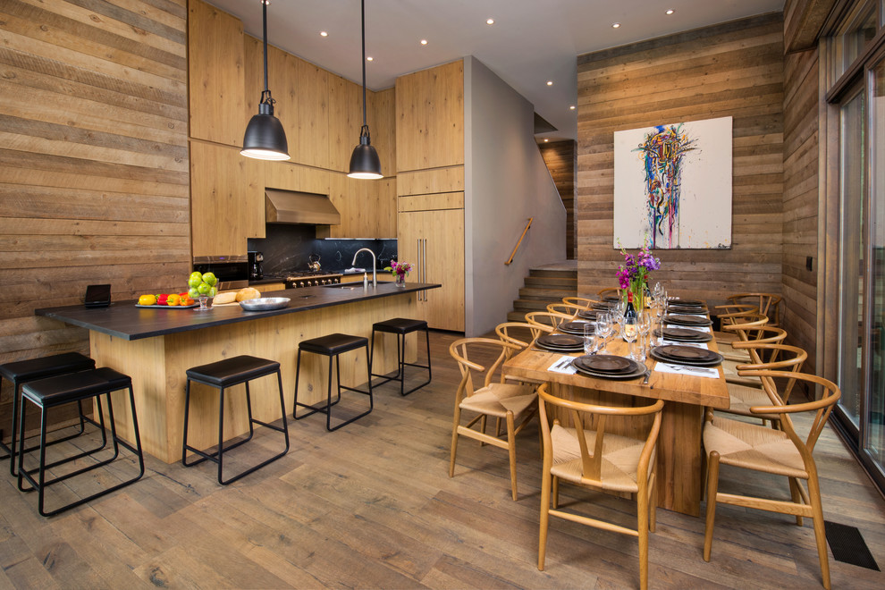 Design ideas for a rustic kitchen/diner in Denver with a submerged sink, flat-panel cabinets, light wood cabinets, black splashback, integrated appliances, medium hardwood flooring, an island and black worktops.