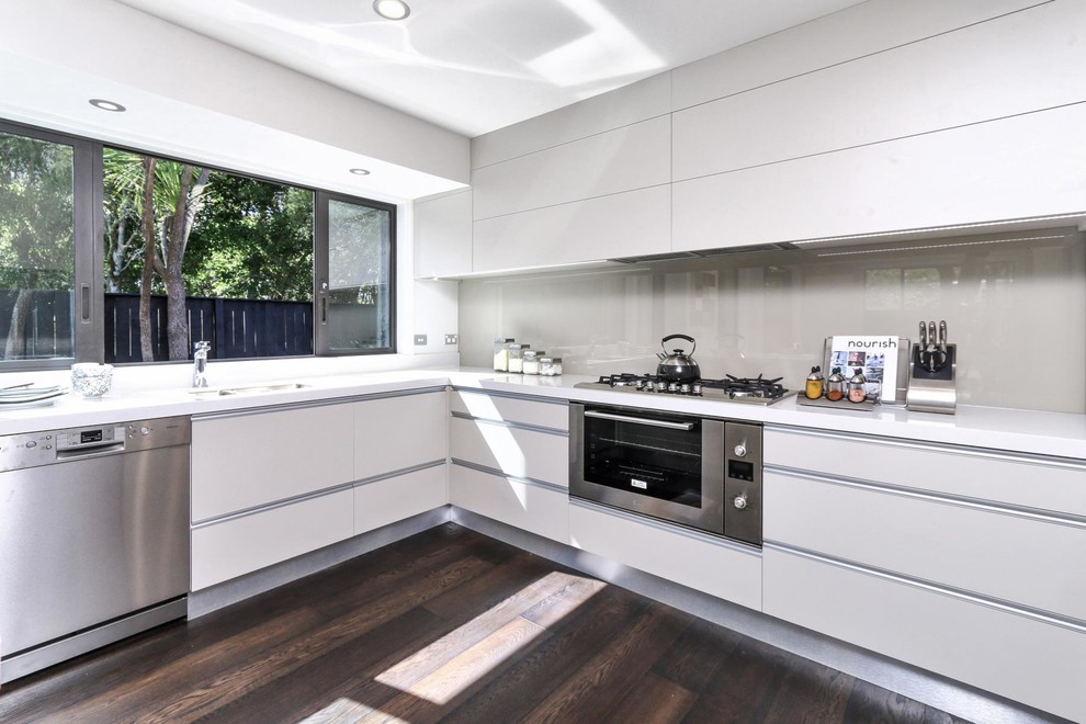 Inspiration for a medium sized modern l-shaped kitchen/diner in Auckland with a double-bowl sink, grey cabinets, granite worktops, grey splashback, glass sheet splashback, stainless steel appliances, dark hardwood flooring, no island and flat-panel cabinets.