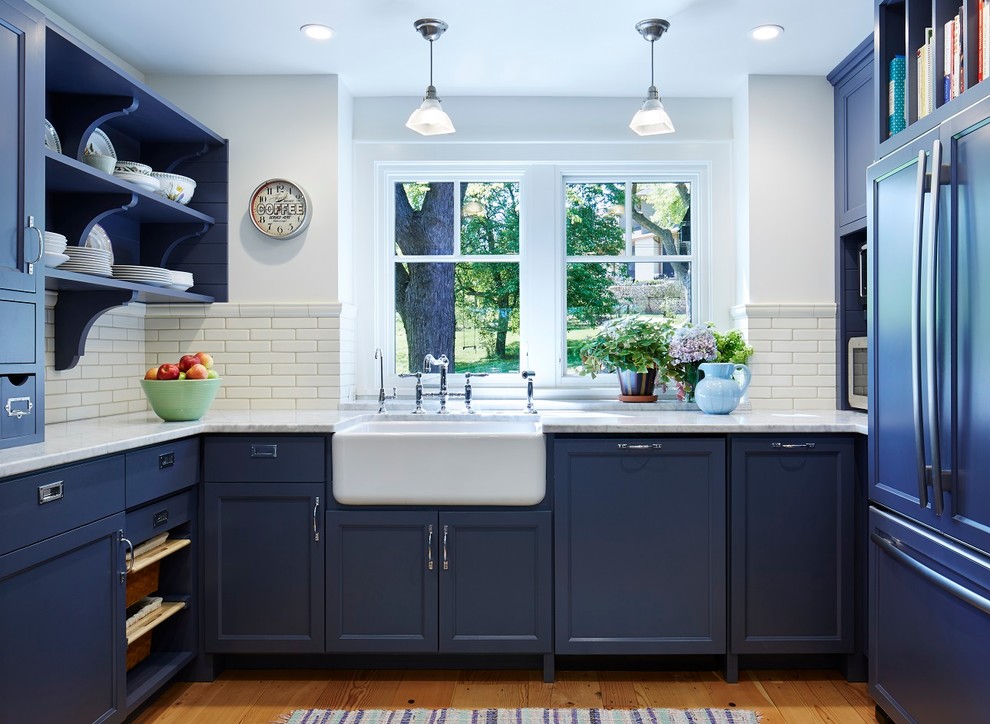 Inspiration for a large timeless u-shaped medium tone wood floor kitchen remodel in Minneapolis with a farmhouse sink, recessed-panel cabinets, blue cabinets, marble countertops, white backsplash, stainless steel appliances and an island