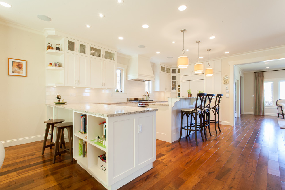This is an example of a traditional kitchen in Vancouver with shaker cabinets, white cabinets, white splashback, metro tiled splashback, integrated appliances, medium hardwood flooring and an island.