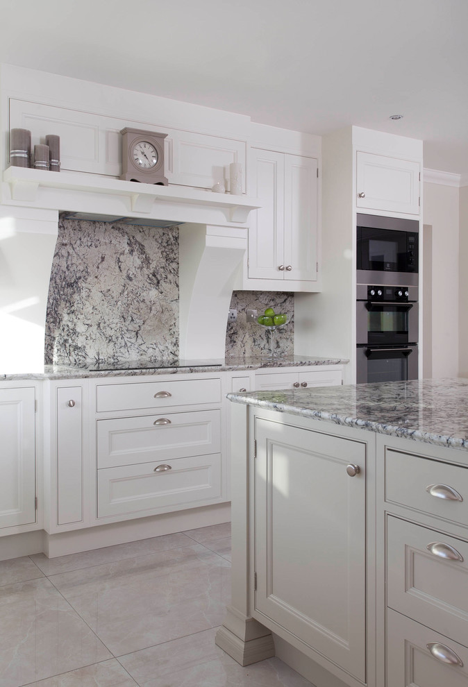 Klassisk inredning av ett stort kök, med en undermonterad diskho, luckor med profilerade fronter, vita skåp, granitbänkskiva, grått stänkskydd, stänkskydd i sten, rostfria vitvaror, klinkergolv i porslin, en köksö och grått golv