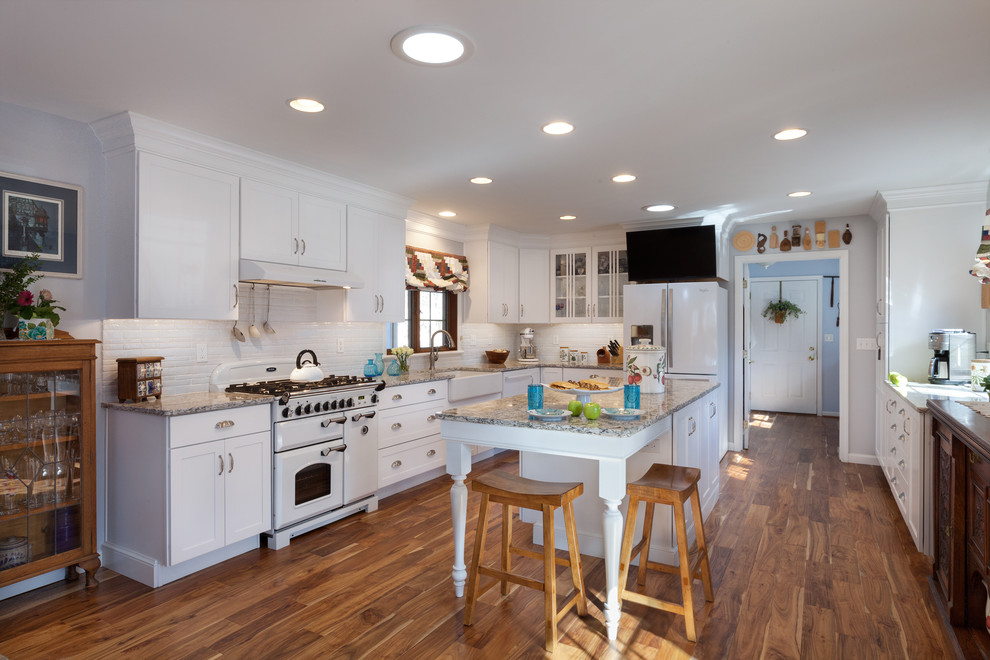 Example of a mid-sized transitional l-shaped medium tone wood floor eat-in kitchen design in Other with a farmhouse sink, white cabinets, quartz countertops, white backsplash, white appliances, an island, recessed-panel cabinets and ceramic backsplash