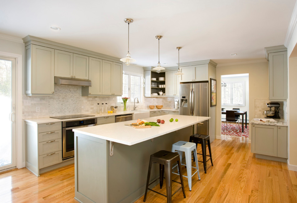Inspiration for a mid-sized transitional l-shaped light wood floor kitchen remodel in Boston with a farmhouse sink, shaker cabinets, gray cabinets, recycled glass countertops, white backsplash, stone tile backsplash, stainless steel appliances and an island