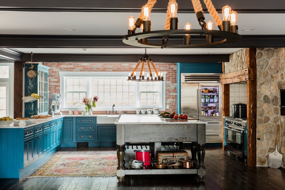 This is an example of an expansive farmhouse galley kitchen/diner in Boston with a belfast sink, glass-front cabinets, turquoise cabinets, engineered stone countertops, red splashback, brick splashback, stainless steel appliances, medium hardwood flooring and an island.