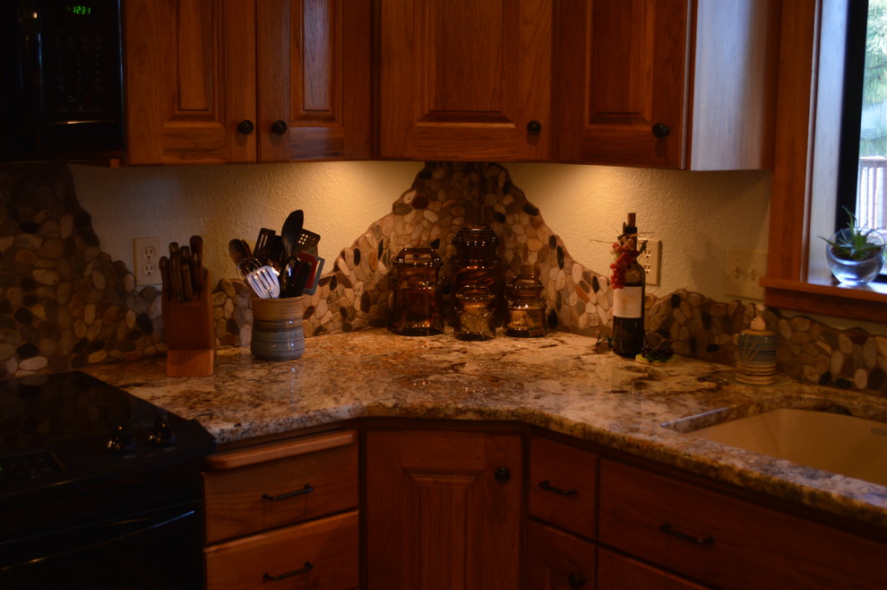 Foto di una cucina stile americano con ante con bugna sagomata, ante in legno scuro, top in granito, paraspruzzi marrone, paraspruzzi con piastrelle a mosaico, elettrodomestici neri e pavimento in legno massello medio