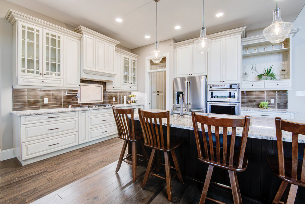 Example of a mid-sized classic single-wall medium tone wood floor and brown floor enclosed kitchen design in Calgary with a double-bowl sink, raised-panel cabinets, white cabinets, granite countertops, brown backsplash, ceramic backsplash, stainless steel appliances, an island and gray countertops