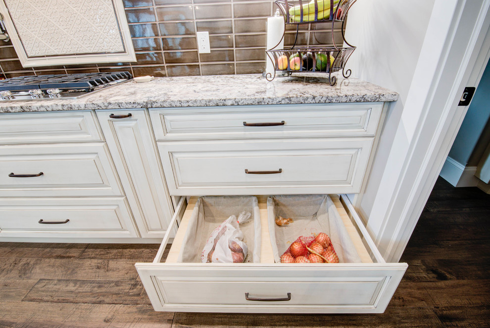 Example of a mid-sized classic single-wall medium tone wood floor and brown floor enclosed kitchen design in Calgary with a double-bowl sink, raised-panel cabinets, white cabinets, granite countertops, brown backsplash, ceramic backsplash, stainless steel appliances, an island and gray countertops