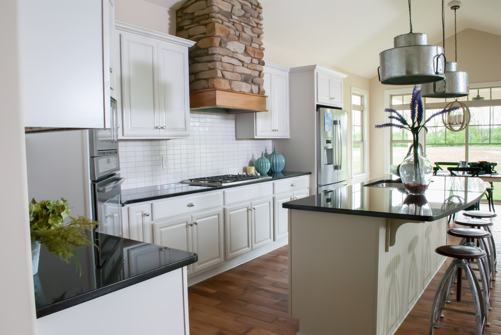 Inspiration for a shabby-chic style l-shaped medium tone wood floor eat-in kitchen remodel in Cleveland with a drop-in sink, raised-panel cabinets, white cabinets, granite countertops, white backsplash, subway tile backsplash, stainless steel appliances and an island