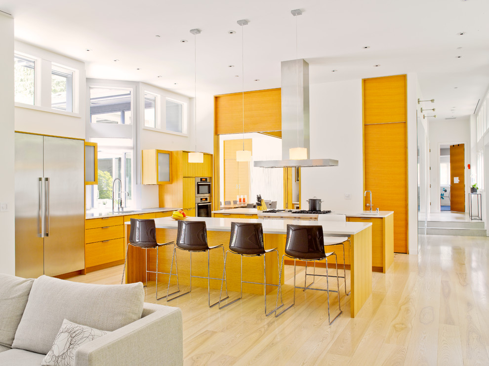 This is an example of a contemporary l-shaped open plan kitchen in Seattle with flat-panel cabinets, medium wood cabinets, stainless steel appliances, a submerged sink, light hardwood flooring and multiple islands.