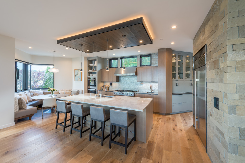 Zweizeilige Moderne Küche mit Landhausspüle, flächenbündigen Schrankfronten, hellbraunen Holzschränken, Küchenrückwand in Grau, Küchengeräten aus Edelstahl, braunem Holzboden, Kücheninsel und braunem Boden in Seattle