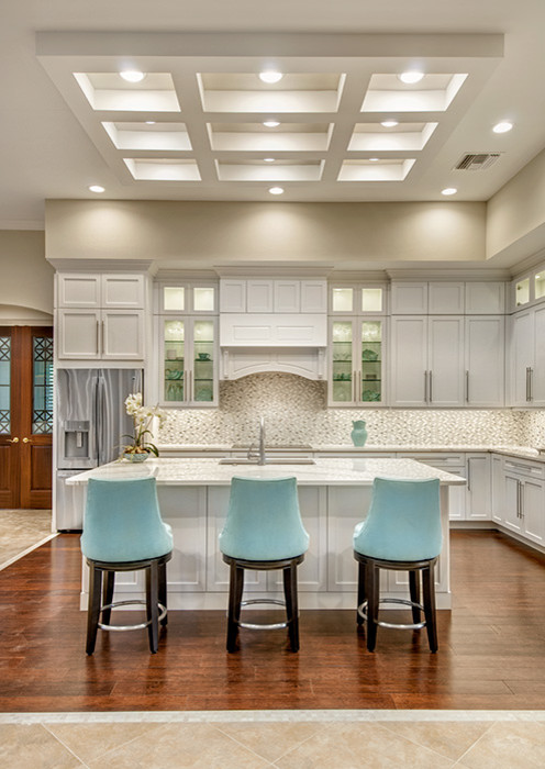 Large transitional l-shaped medium tone wood floor open concept kitchen photo in Miami with an undermount sink, shaker cabinets, white cabinets, quartz countertops, white backsplash, mosaic tile backsplash, stainless steel appliances and an island