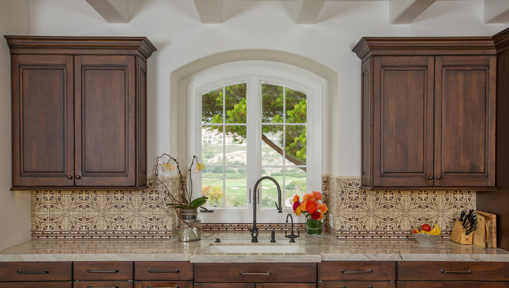 Inspiration for a large mediterranean single-wall travertine floor eat-in kitchen remodel in Orange County with an undermount sink, raised-panel cabinets, dark wood cabinets, marble countertops, beige backsplash, mosaic tile backsplash and stainless steel appliances