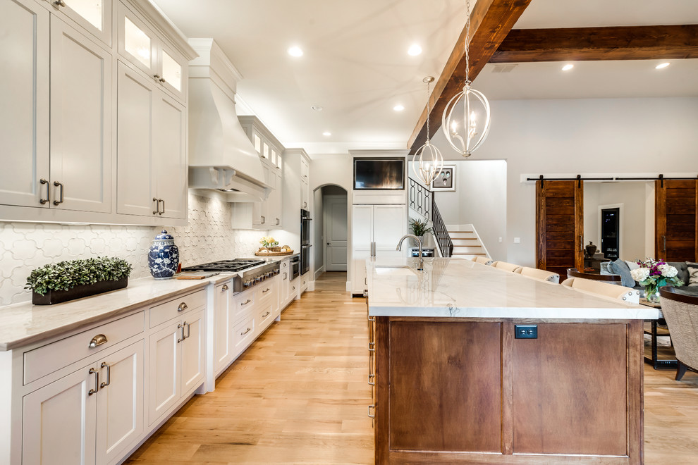 Large tuscan l-shaped light wood floor eat-in kitchen photo in Dallas with an undermount sink, shaker cabinets, white cabinets, quartzite countertops, white backsplash, ceramic backsplash, white appliances and an island