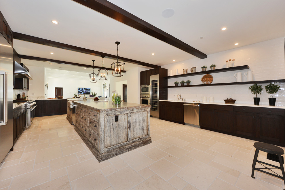 Inspiration for a huge mediterranean u-shaped travertine floor and beige floor open concept kitchen remodel in Los Angeles with a farmhouse sink, shaker cabinets, brown cabinets, white backsplash, stone slab backsplash, stainless steel appliances, an island and white countertops