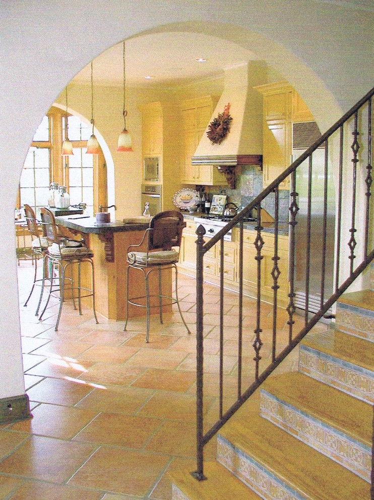 Exempel på ett klassiskt kök, med en rustik diskho, luckor med profilerade fronter, gula skåp, kaklad bänkskiva, grått stänkskydd, stänkskydd i stenkakel, rostfria vitvaror, klinkergolv i keramik och en köksö