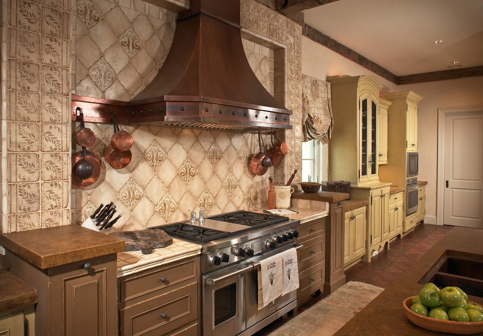На фото: кухня в средиземноморском стиле с фасадами с утопленной филенкой, коричневыми фасадами, бежевым фартуком и техникой из нержавеющей стали с
