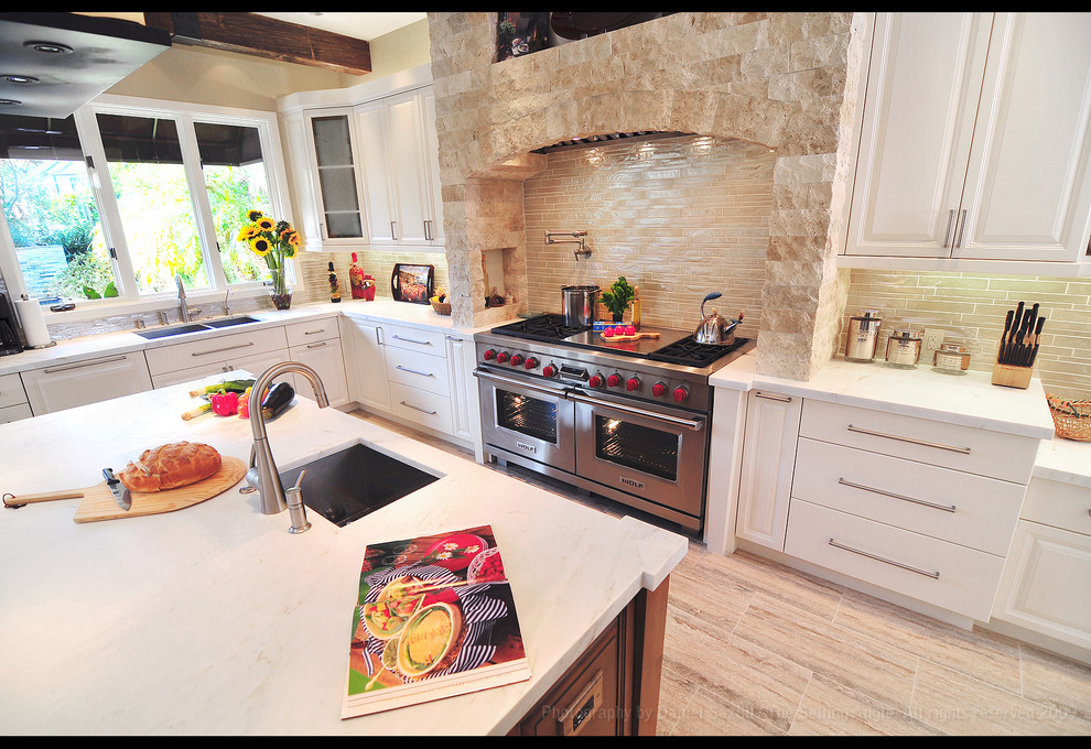 ロサンゼルスにある高級な広い地中海スタイルのおしゃれなキッチン (ダブルシンク、レイズドパネル扉のキャビネット、白いキャビネット、大理石カウンター、ベージュキッチンパネル、石タイルのキッチンパネル、シルバーの調理設備、淡色無垢フローリング) の写真
