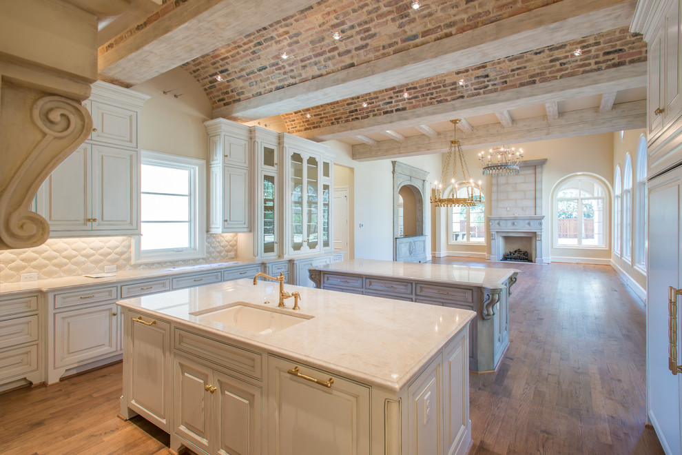 Large tuscan u-shaped medium tone wood floor and brown floor eat-in kitchen photo in Dallas with a double-bowl sink, recessed-panel cabinets, distressed cabinets, marble countertops, white backsplash, porcelain backsplash and two islands