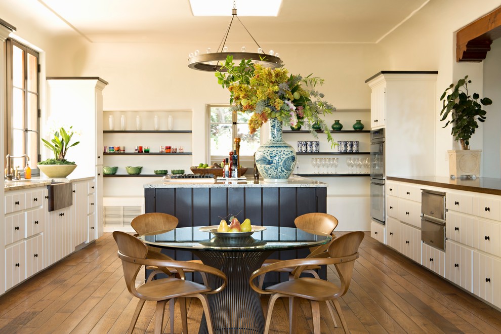 Inspiration for a mediterranean u-shaped kitchen/diner in Portland with a belfast sink, flat-panel cabinets, white cabinets, stainless steel appliances, dark hardwood flooring and an island.