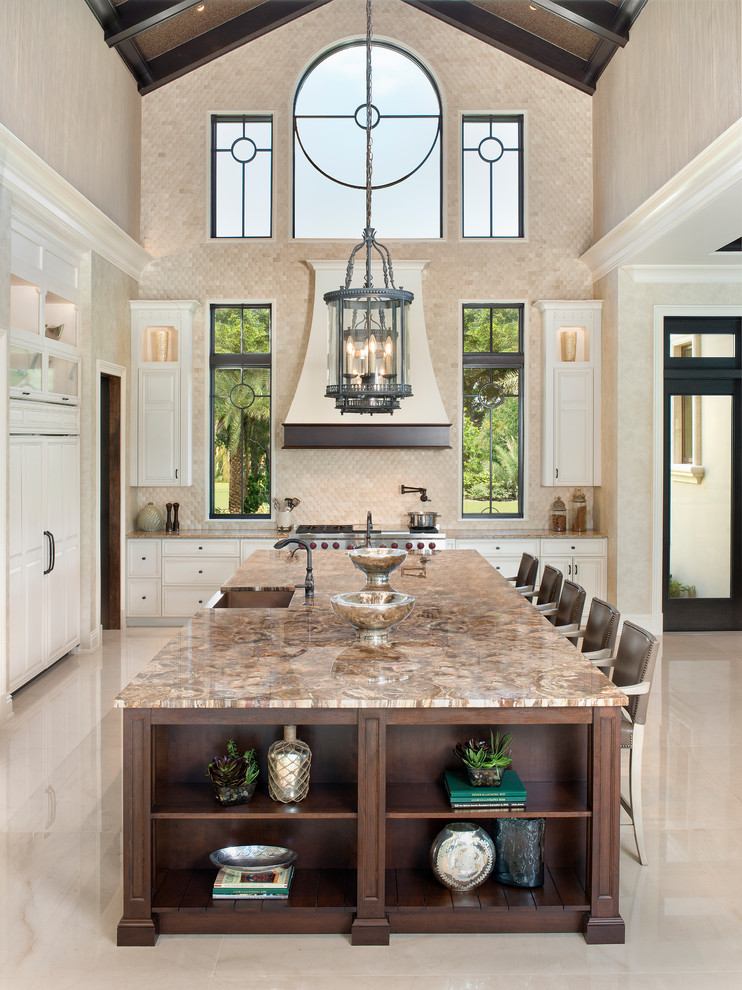 This is an example of a mediterranean kitchen in Other with a submerged sink, recessed-panel cabinets, white cabinets, beige splashback, stainless steel appliances, an island and beige floors.
