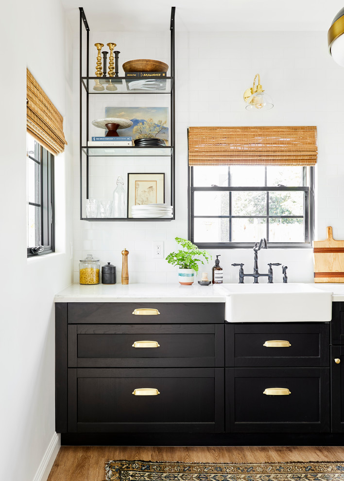 Exempel på ett litet medelhavsstil vit vitt kök med öppen planlösning, med en rustik diskho, skåp i shakerstil, svarta skåp, bänkskiva i kvarts, vitt stänkskydd, stänkskydd i keramik, rostfria vitvaror, ljust trägolv, en köksö och brunt golv