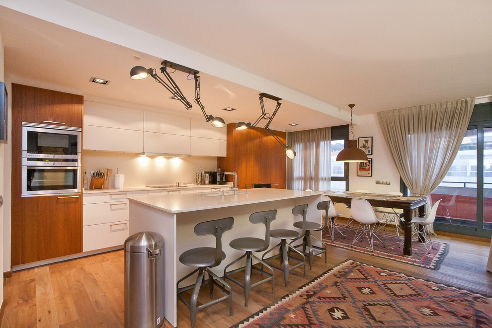 Inspiration for a large contemporary single-wall medium tone wood floor eat-in kitchen remodel in Barcelona with flat-panel cabinets, white cabinets, white backsplash, stainless steel appliances, an island and an undermount sink
