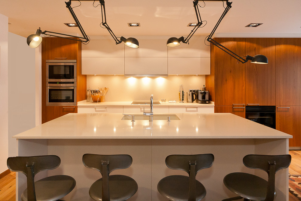 Inredning av ett modernt mellanstort linjärt kök med öppen planlösning, med en köksö, släta luckor, vita skåp, bänkskiva i kvarts, vitt stänkskydd, rostfria vitvaror, mellanmörkt trägolv och en undermonterad diskho