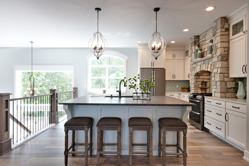 Bild på ett avskilt lantligt grå grått l-kök, med luckor med infälld panel, vita skåp, blått stänkskydd, rostfria vitvaror, mellanmörkt trägolv, en köksö och brunt golv