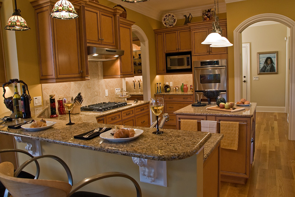 Mid-sized tuscan u-shaped medium tone wood floor eat-in kitchen photo in Charlotte with an undermount sink, recessed-panel cabinets, medium tone wood cabinets, granite countertops, beige backsplash, porcelain backsplash, stainless steel appliances and an island