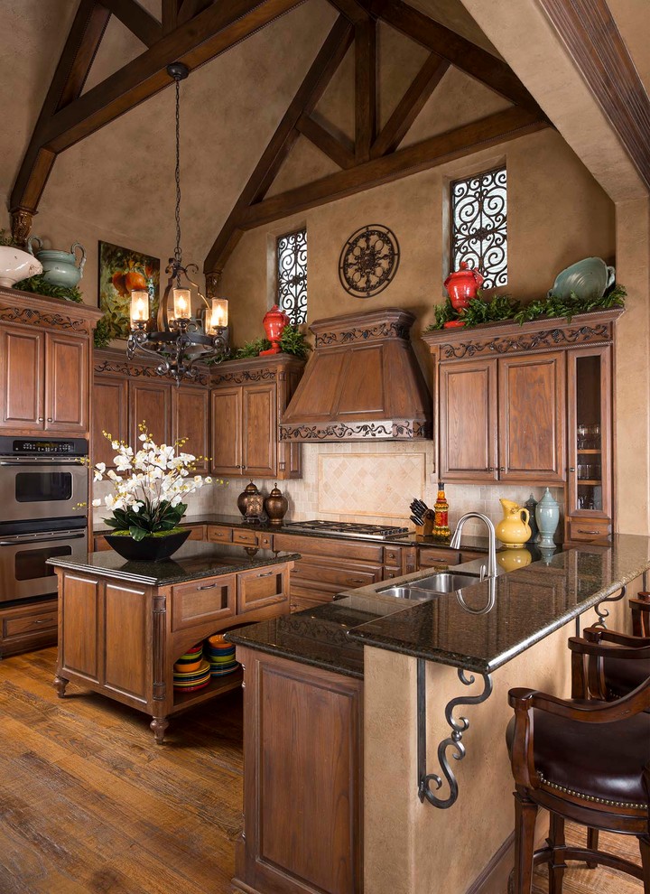 Example of a mid-sized tuscan u-shaped medium tone wood floor eat-in kitchen design in Other with a double-bowl sink, raised-panel cabinets, medium tone wood cabinets, beige backsplash, stainless steel appliances and two islands