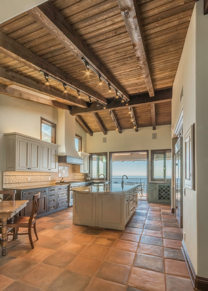 Example of a large tuscan u-shaped terra-cotta tile eat-in kitchen design in Orange County with a farmhouse sink, beaded inset cabinets, white cabinets, granite countertops, multicolored backsplash, stone tile backsplash, stainless steel appliances and an island